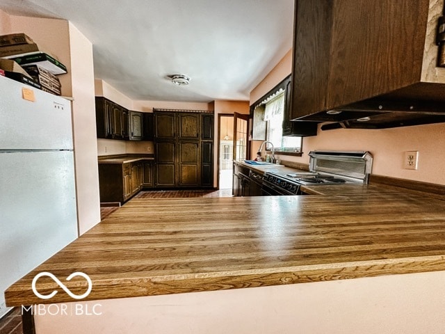 kitchen with white refrigerator, custom exhaust hood, sink, dark brown cabinetry, and stainless steel range