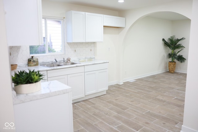 kitchen with white cabinetry, sink, backsplash, and light wood-type flooring