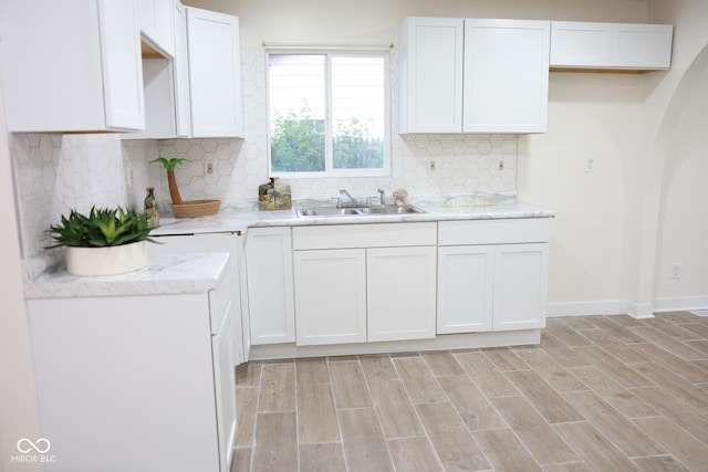 kitchen with white cabinetry, light wood-type flooring, sink, and backsplash