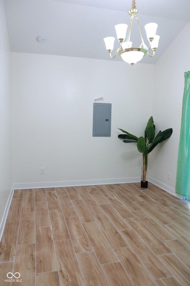 empty room featuring a notable chandelier, electric panel, and light hardwood / wood-style floors