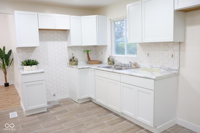 kitchen featuring tasteful backsplash, white cabinetry, sink, and light stone counters