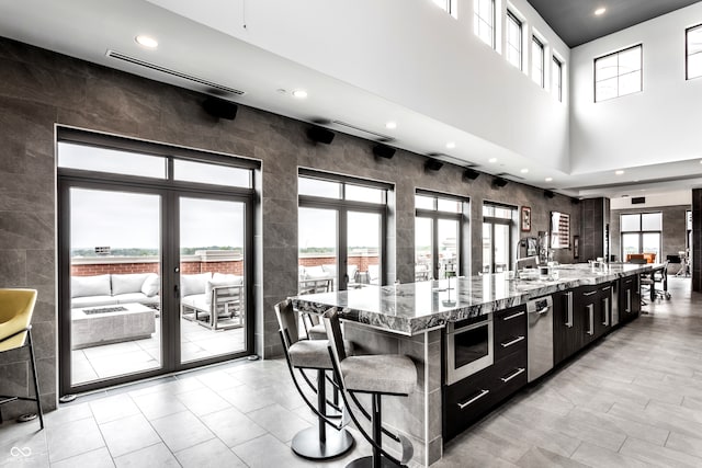 kitchen with light tile patterned floors, a high ceiling, a large island, light stone counters, and a kitchen bar