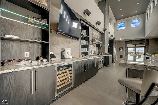 kitchen with range with two ovens, a towering ceiling, light stone countertops, and wine cooler