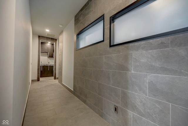 hall with light tile patterned flooring and tile walls