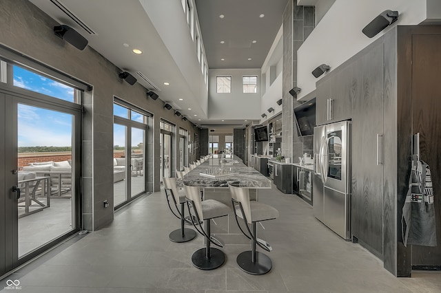 interior space with plenty of natural light, light stone counters, stainless steel refrigerator with ice dispenser, and a high ceiling