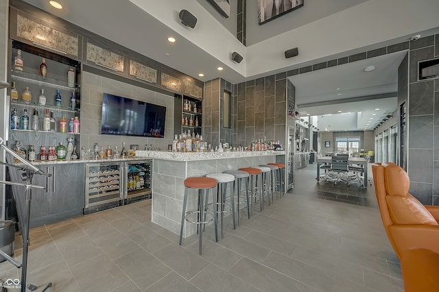 bar featuring light tile patterned flooring, beverage cooler, tile walls, and light stone countertops