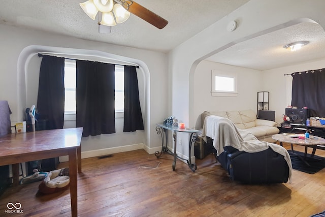 living room featuring wood-type flooring, ceiling fan, and a textured ceiling