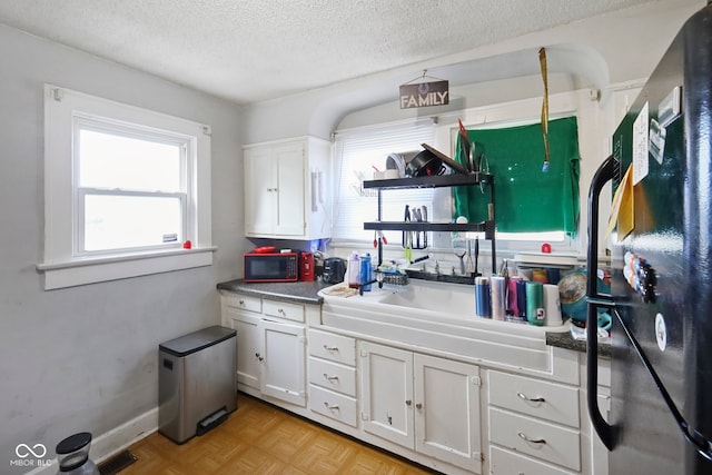 kitchen with a textured ceiling, light parquet flooring, and white cabinetry