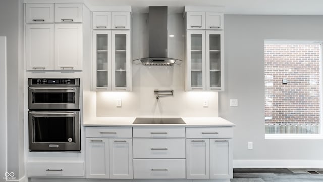 kitchen featuring a healthy amount of sunlight, stainless steel double oven, wall chimney exhaust hood, and black electric stovetop