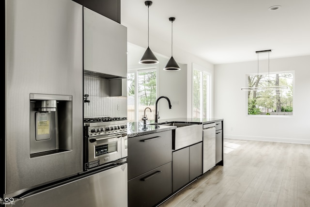 kitchen with dark stone counters, pendant lighting, sink, dishwasher, and light hardwood / wood-style floors