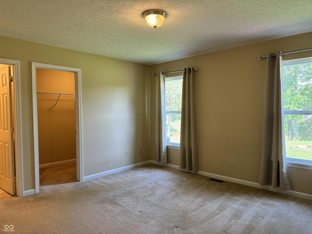 unfurnished bedroom with a walk in closet, light colored carpet, and multiple windows