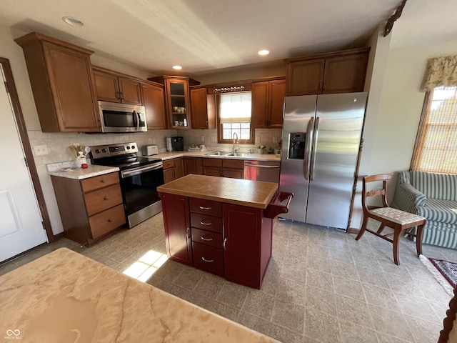 kitchen featuring backsplash, appliances with stainless steel finishes, glass insert cabinets, a kitchen island, and a sink