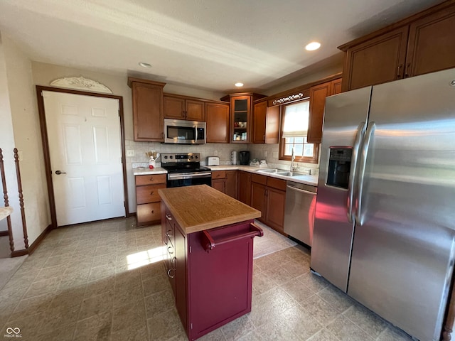 kitchen with appliances with stainless steel finishes, backsplash, light tile patterned floors, sink, and a kitchen island