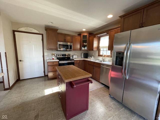 kitchen featuring appliances with stainless steel finishes, brown cabinetry, glass insert cabinets, a kitchen island, and a sink