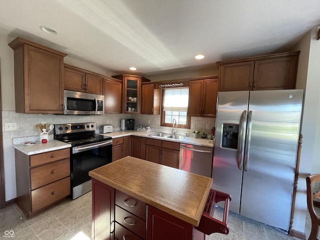 kitchen featuring stainless steel appliances, a sink, light countertops, decorative backsplash, and glass insert cabinets