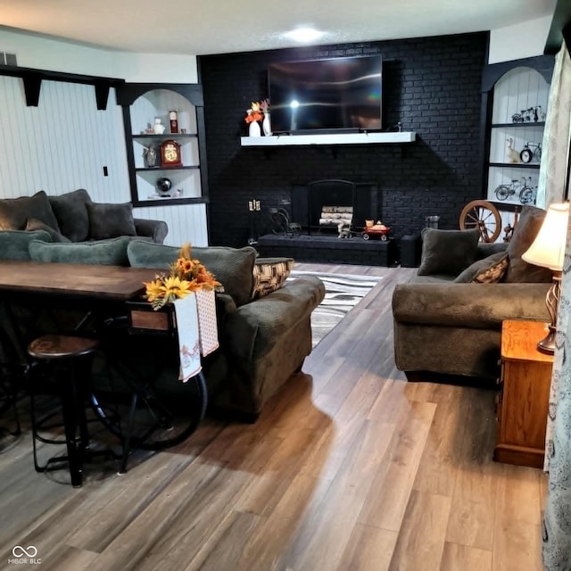 living room featuring built in features, wood-type flooring, and a brick fireplace