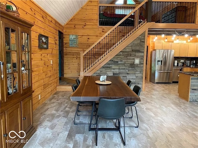 dining area featuring high vaulted ceiling and wooden walls