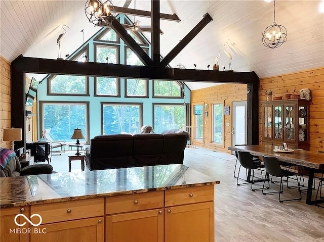 kitchen with a notable chandelier, high vaulted ceiling, light stone countertops, wood walls, and light hardwood / wood-style flooring