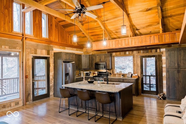 kitchen with wooden ceiling, light wood-style flooring, appliances with stainless steel finishes, light stone countertops, and beamed ceiling