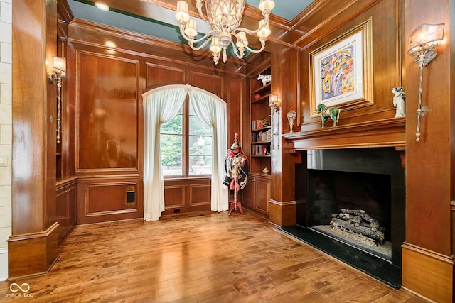 interior space featuring wood-type flooring, crown molding, wooden walls, and an inviting chandelier