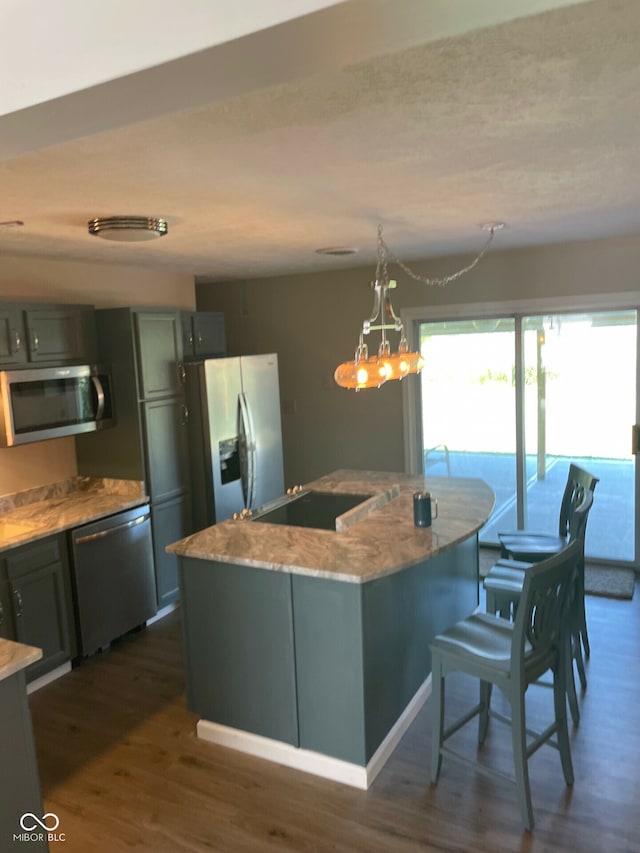 kitchen with light stone countertops, dark hardwood / wood-style flooring, decorative light fixtures, a kitchen island with sink, and appliances with stainless steel finishes