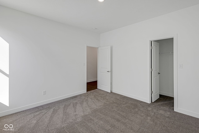 unfurnished bedroom featuring dark carpet, a walk in closet, and a closet