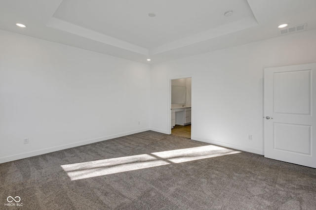 spare room with dark colored carpet and a tray ceiling