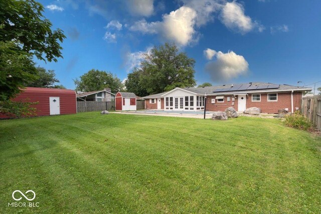 rear view of property featuring solar panels, a storage unit, and a lawn