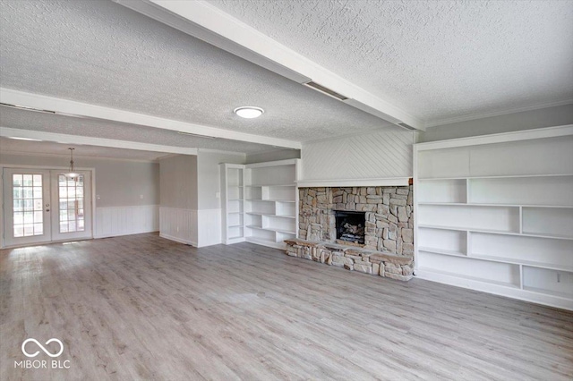 unfurnished living room featuring beamed ceiling, hardwood / wood-style floors, a stone fireplace, french doors, and a textured ceiling