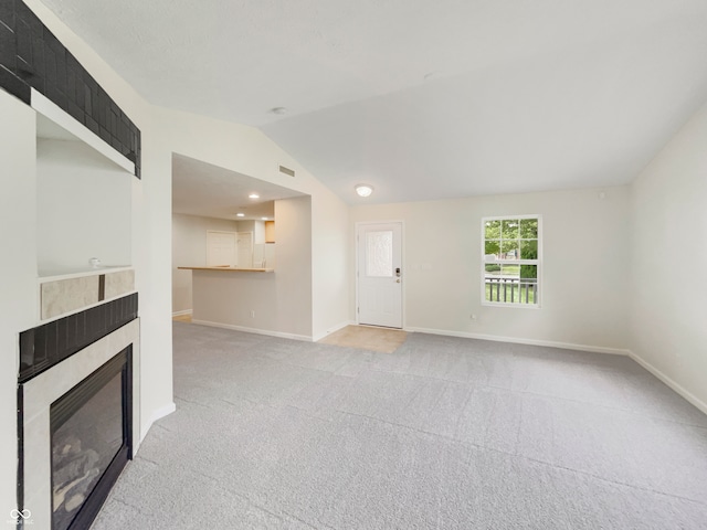 unfurnished living room with lofted ceiling, a tiled fireplace, and carpet floors