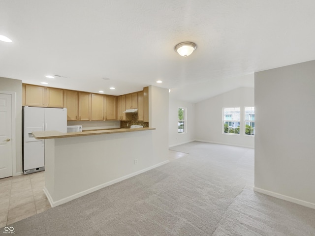 kitchen featuring white appliances, light carpet, vaulted ceiling, kitchen peninsula, and light brown cabinets