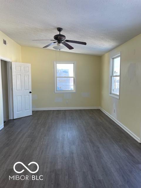 spare room with a textured ceiling, dark wood-type flooring, and a healthy amount of sunlight