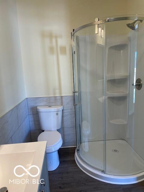 bathroom featuring an enclosed shower, vanity, hardwood / wood-style flooring, tile walls, and toilet