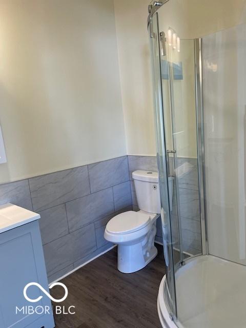 bathroom with vanity, a shower with door, hardwood / wood-style flooring, toilet, and tile walls