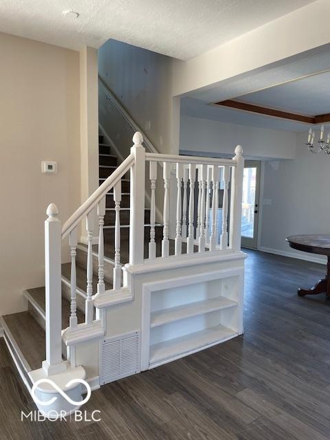 stairway featuring wood-type flooring, a textured ceiling, and an inviting chandelier