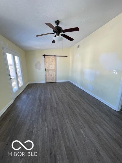 spare room with a barn door, ceiling fan, french doors, and dark wood-type flooring