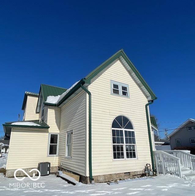 snow covered rear of property featuring central AC