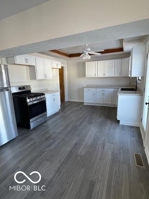 kitchen featuring ceiling fan, stainless steel appliances, a raised ceiling, dark hardwood / wood-style flooring, and white cabinets