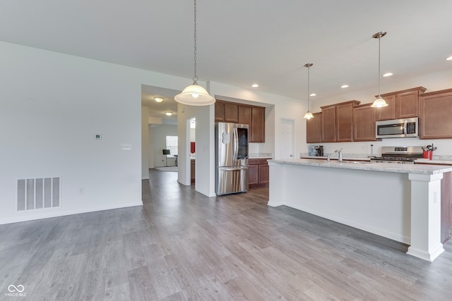 kitchen with hardwood / wood-style floors, pendant lighting, an island with sink, sink, and stainless steel appliances