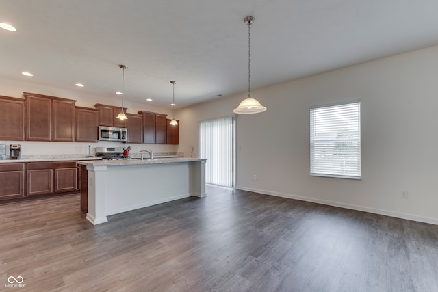 kitchen with pendant lighting, a wealth of natural light, a kitchen island with sink, and appliances with stainless steel finishes