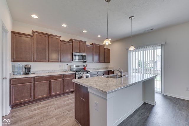 kitchen with sink, light hardwood / wood-style flooring, appliances with stainless steel finishes, an island with sink, and decorative light fixtures