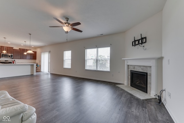 unfurnished living room featuring a tiled fireplace, dark hardwood / wood-style floors, and ceiling fan