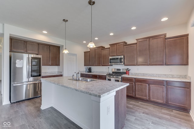 kitchen featuring appliances with stainless steel finishes, decorative light fixtures, sink, hardwood / wood-style flooring, and a kitchen island with sink