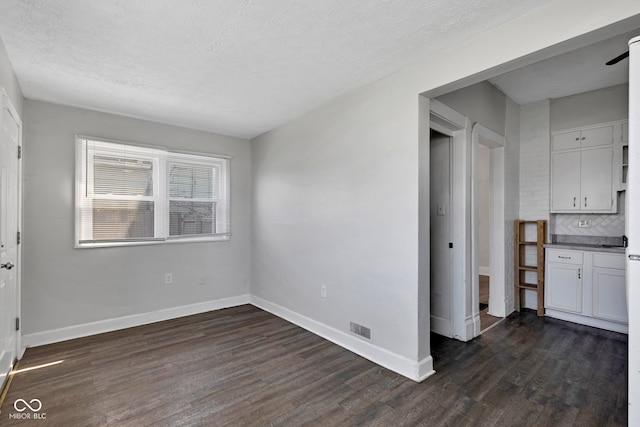 unfurnished room with a textured ceiling, dark wood-style flooring, baseboards, and visible vents