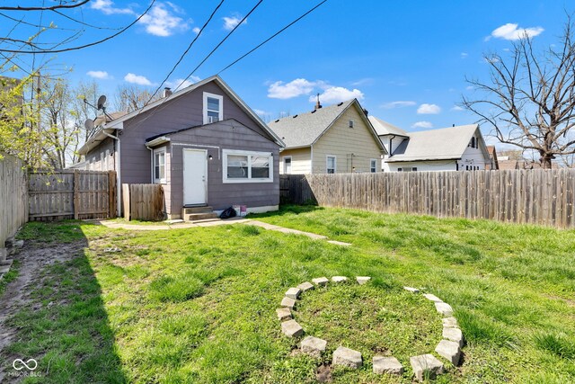 rear view of property with entry steps, a fenced backyard, and a lawn