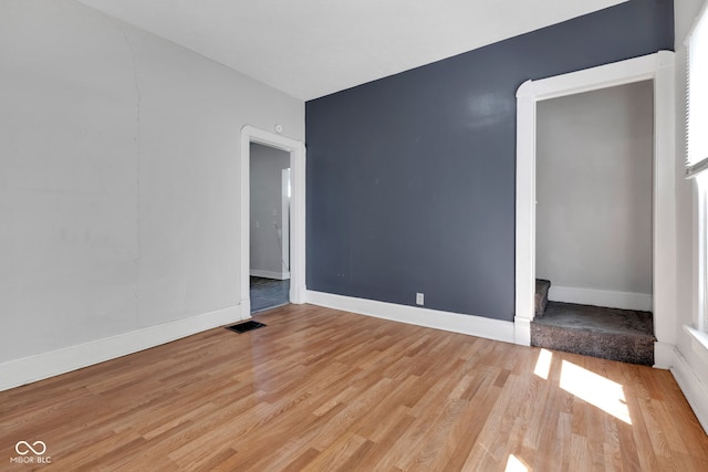 empty room with light wood-style floors, stairway, visible vents, and baseboards