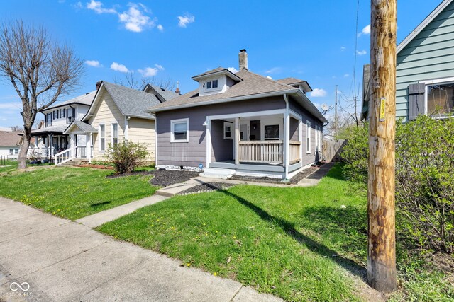 bungalow-style house featuring roof with shingles, a front lawn, covered porch, and a chimney