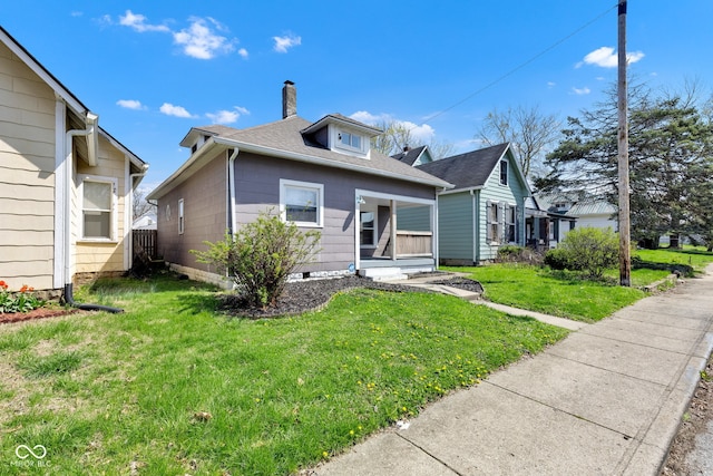 bungalow-style home with roof with shingles, a front lawn, and a chimney