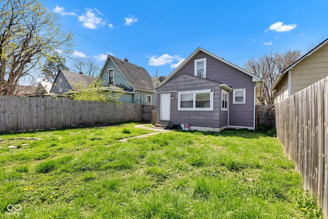 rear view of property with entry steps, a fenced backyard, and a lawn