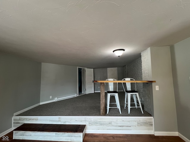 interior space featuring wood-type flooring, baseboard heating, and brick wall